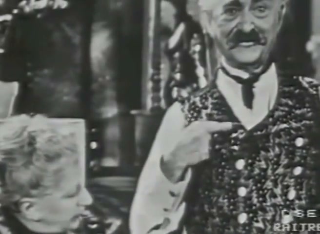 Gilberto Govi, in gilet, indica col dito l'asola in alto; accanto Rina Gaioni